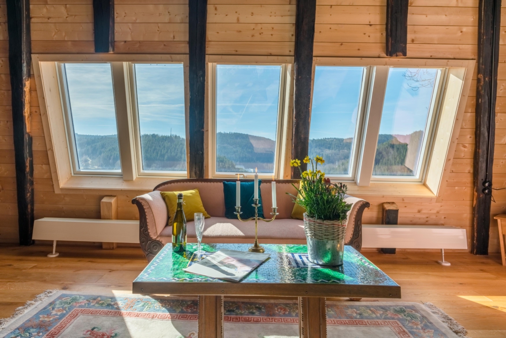 Couchtisch mit Sofa vor 5 großen Panoramadachfenstern mit Aussicht auf bewaldete Hügel