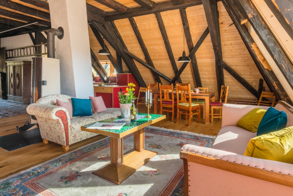 Blick in den Raum mit Sofaecke- Kaminofen und im Hintergrund Esstisch für 6 Personen und Küchenbereich