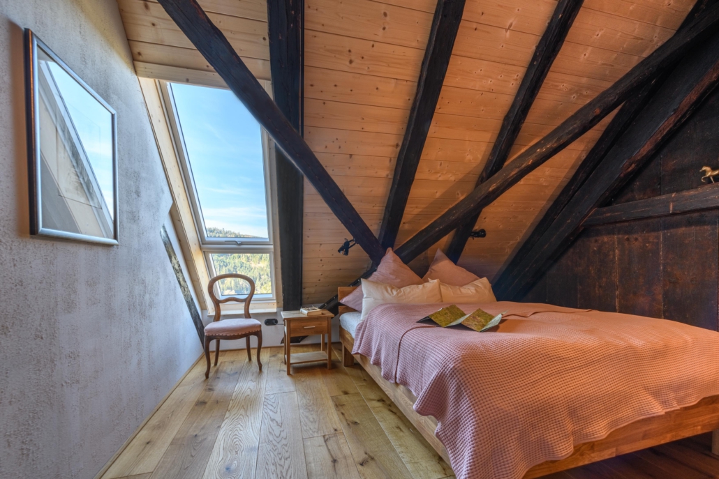 Doppelbett im Schlafzimmer unter dem alten Dachgebälk neben dem Dachfenster